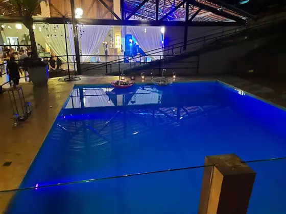 Piscina iluminada em azul, à noite, ao lado do salão